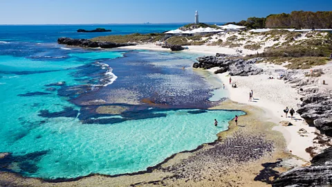 Tourism Western Australia People on beach at the Basin, Rottnest Island with a lighthouse in the background (Credit: Tourism Western Australia)